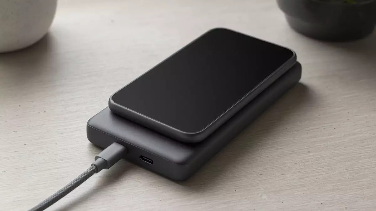 A dark phone with a black screen rests on a dark power bank, with one cable seated in the near port.